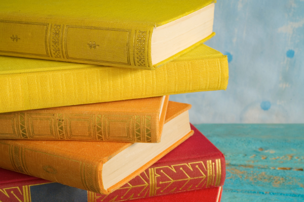 A stack of personal growth books.  Image of a stack of books with yellow, orange, and red covers resting on a turquois blue table.